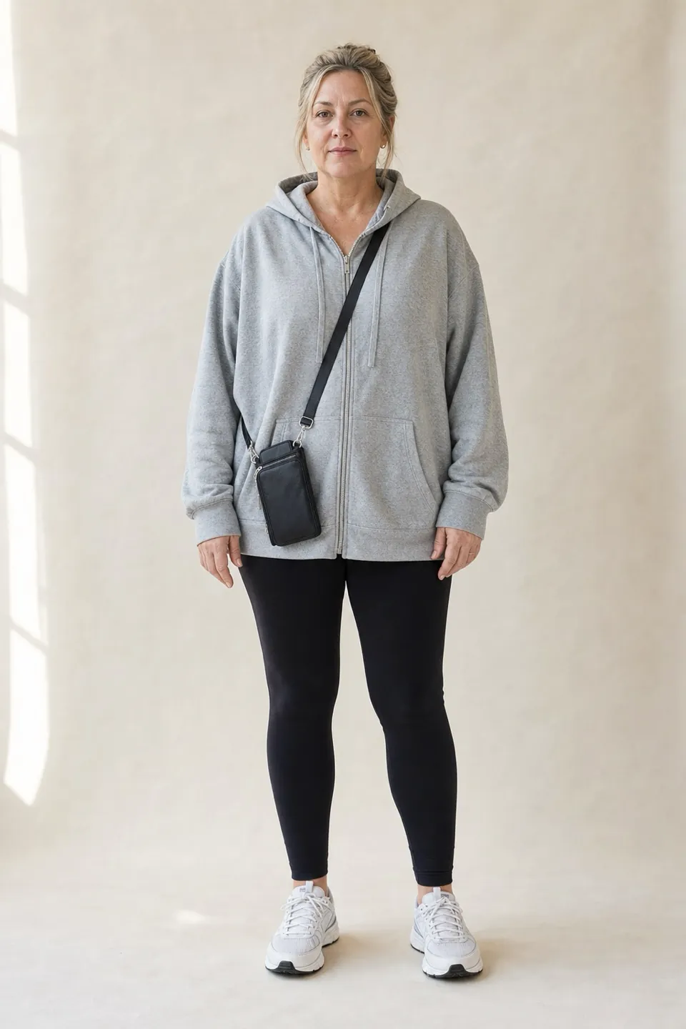 A woman in her fifties in an oversized gray hoodie, black leggings and white running sneakers